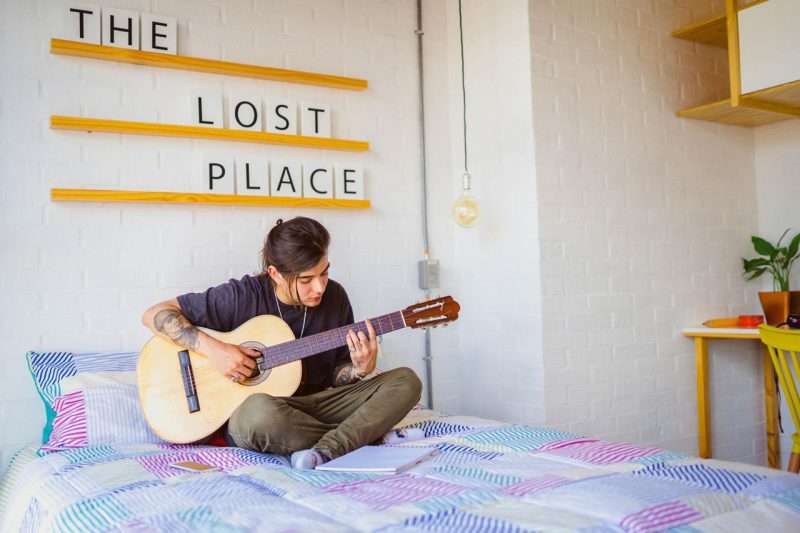 A girl is playing the guitar on a bed in a beautiful modern Indie studio in Laureles, Medellin. VICO rent a room in Medellin